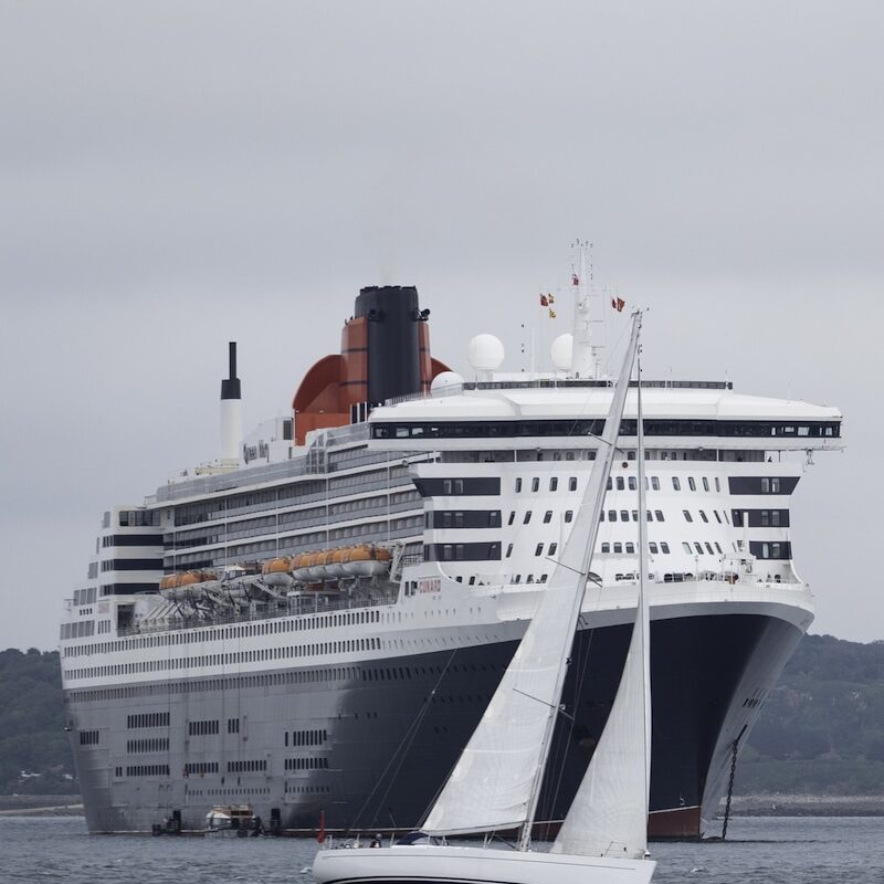 Queen Mary 2 mit Segelboot in Landnähe